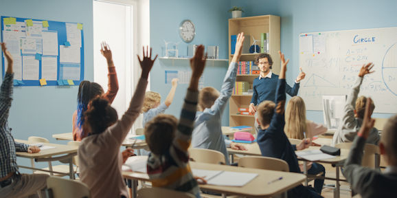 Classroom full of children holding up their hands
